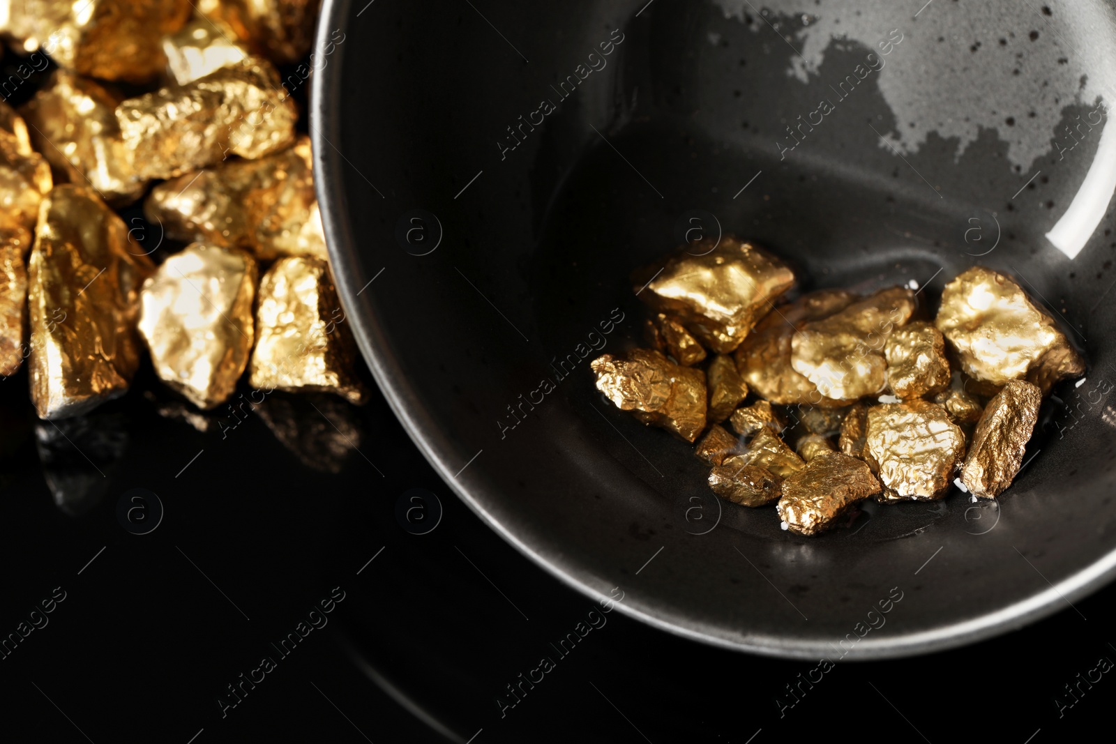 Photo of Bowl with gold nuggets on black background, closeup