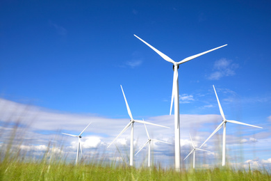 Image of Alternative energy source. Wind turbines in field under blue sky, low angle view
