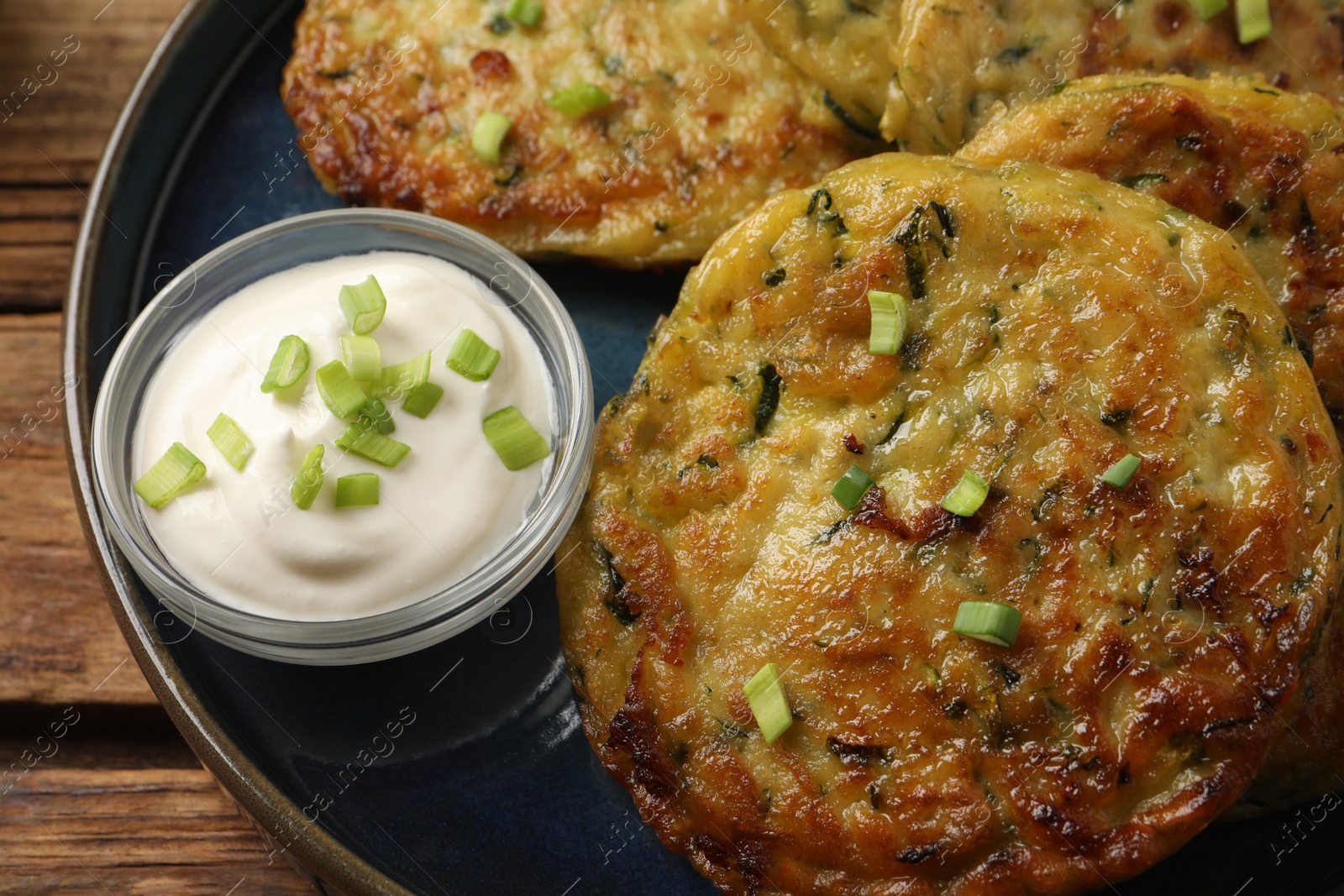 Photo of Delicious zucchini fritters with sour cream served on wooden table, above view