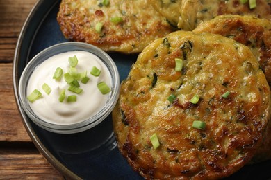 Delicious zucchini fritters with sour cream served on wooden table, above view