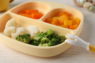 Baby food. Section plate with different vegetables on white wooden table, closeup