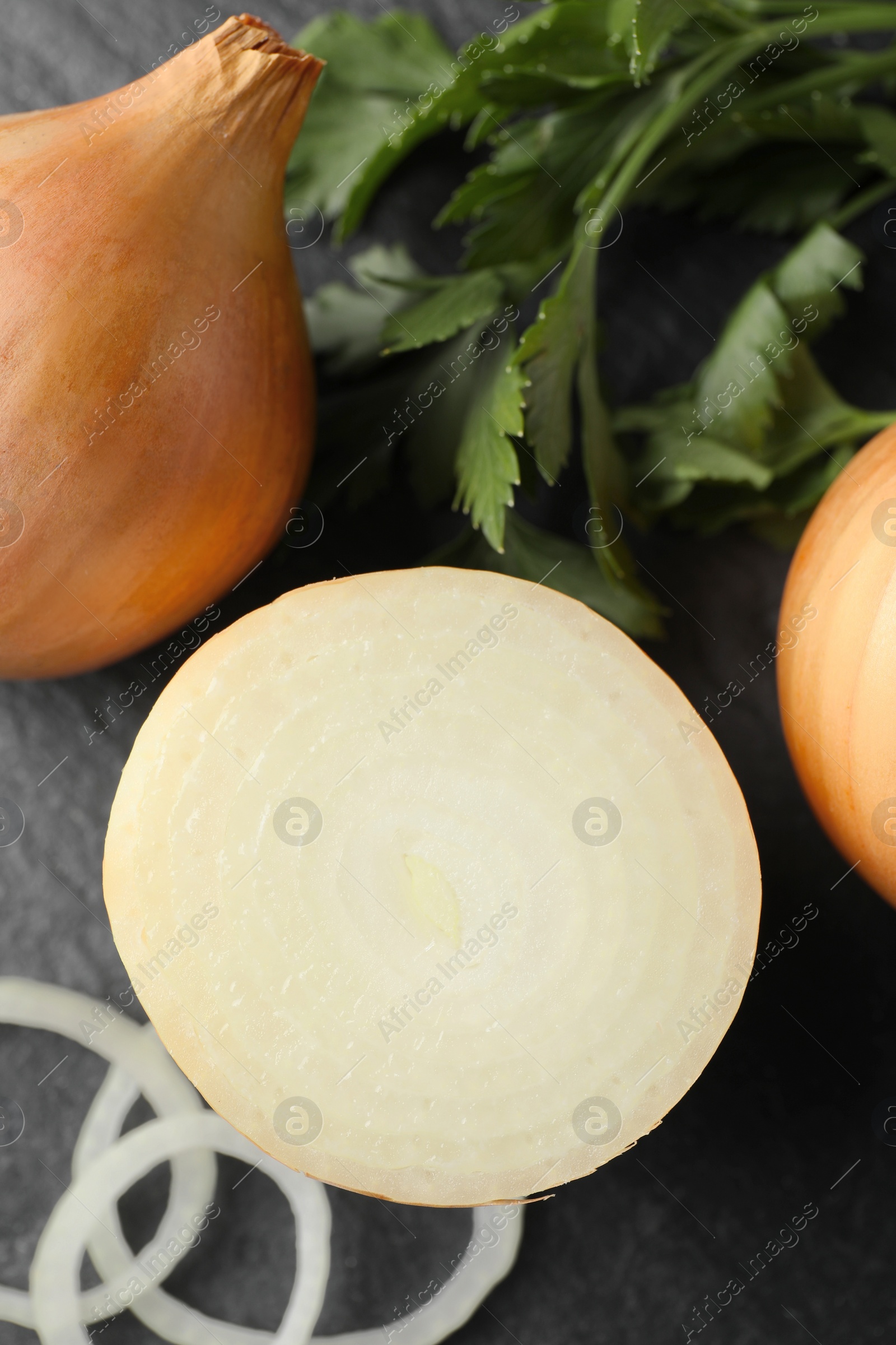 Photo of Whole and cut onions with parsley on black textured table, flat lay