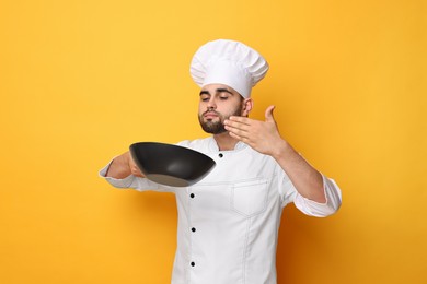 Professional chef smelling something in wok on yellow background