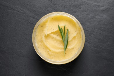 Body scrub and rosemary in jar on black table, top view