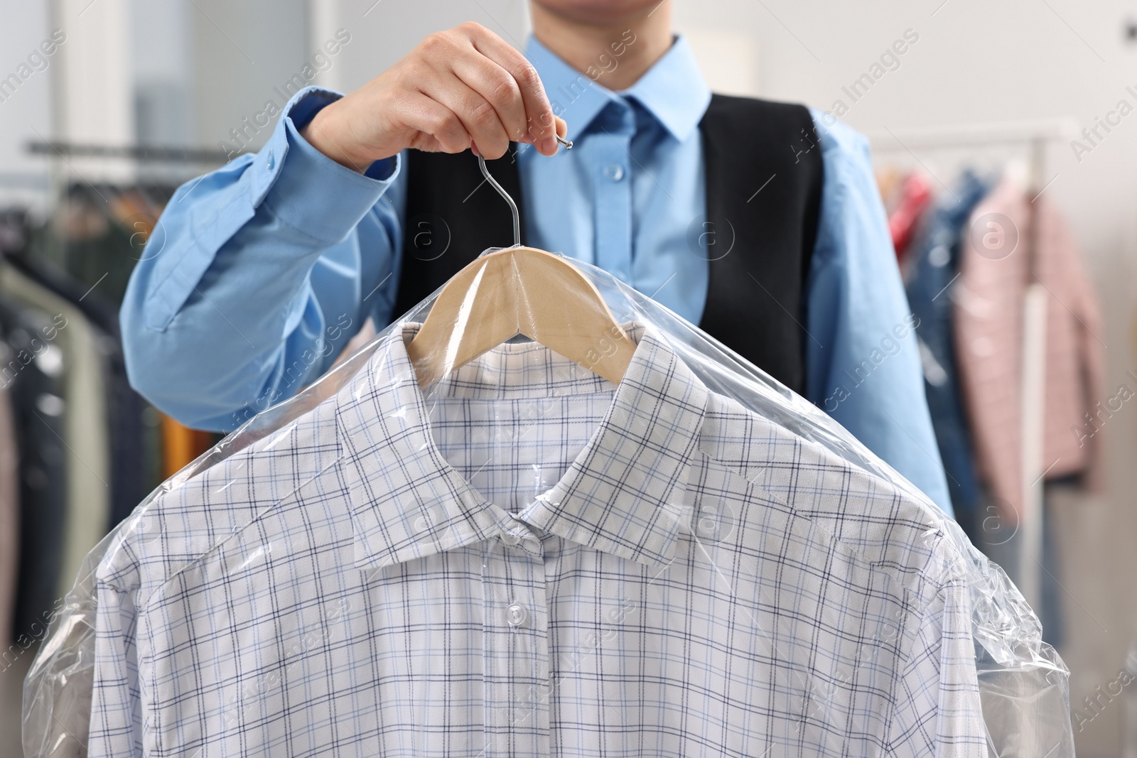 Photo of Dry-cleaning service. Woman holding shirt in plastic bag indoors, closeup