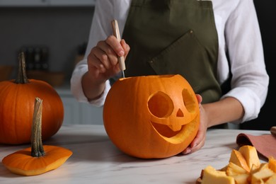 Woman carving pumpkin for Halloween at white marble table in kitchen, closeup