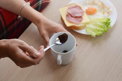 Woman making morning coffee while having breakfast at wooden table, closeup