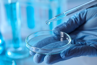 Scientist dripping liquid from pipette into petri dish in laboratory, closeup