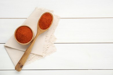Bowl and spoon with aromatic paprika powder on white wooden table, flat lay. Space for text