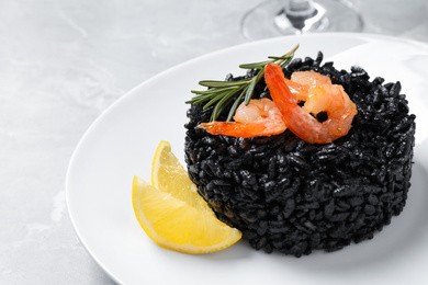 Photo of Delicious black risotto with shrimps and lemon on marble table, closeup