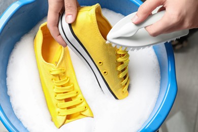 Photo of Woman cleaning stylish sneakers with brush in wash basin, top view