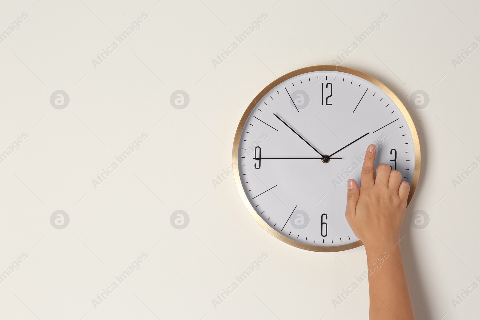 Photo of Woman touching clock on light wall, space for text. Time management