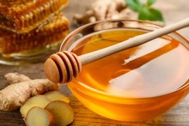 Photo of Honey in bowl and ginger on wooden table, closeup. Natural cold remedies