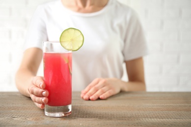 Photo of Young woman with glass of tasty refreshing drink at wooden table, closeup