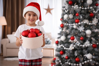 Photo of Cute little girl holding box with Christmas balls at home