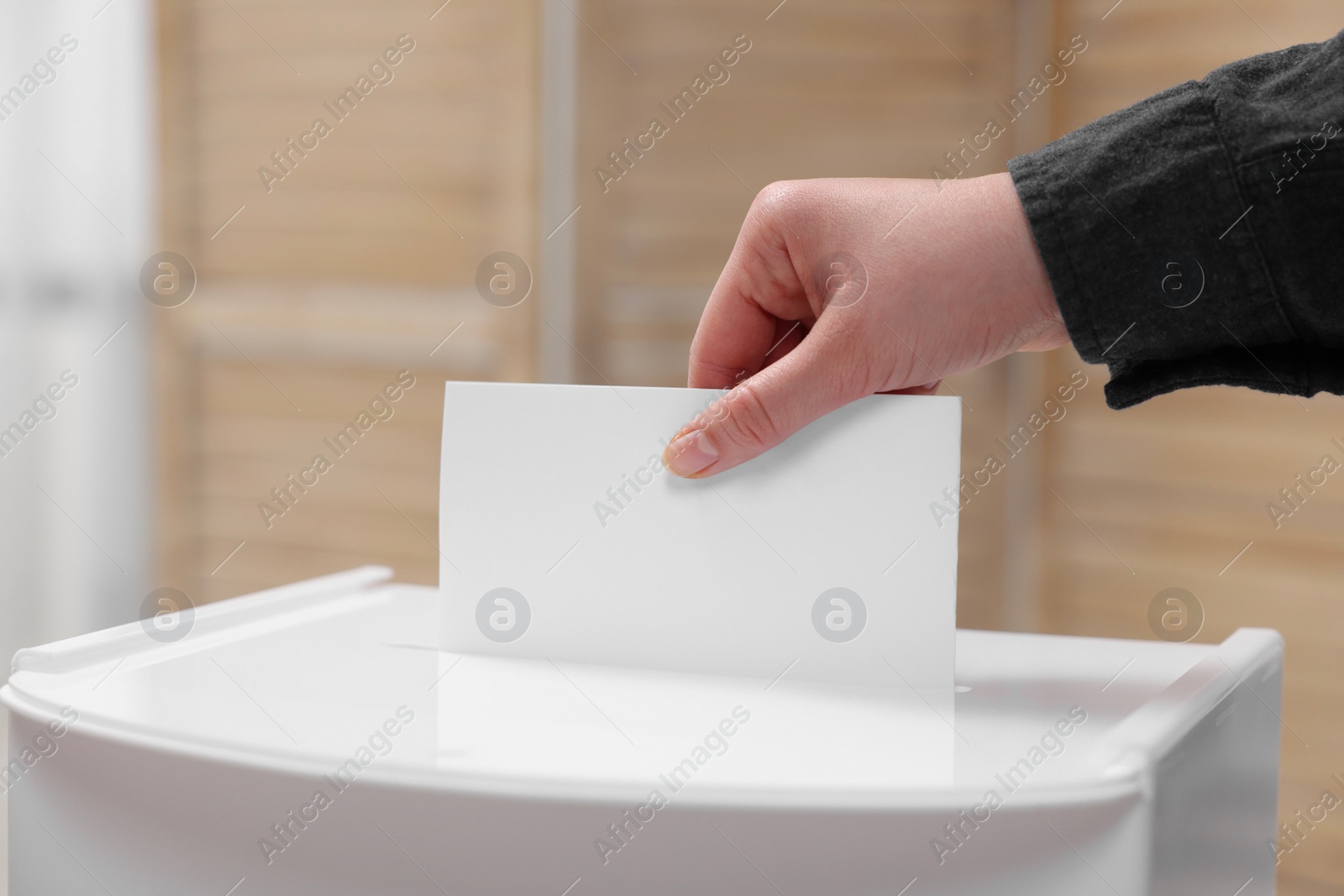 Photo of Woman putting her vote into ballot box on blurred background, closeup