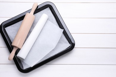 Baking pan with parchment paper and rolling pin on white wooden table, top view. Space for text