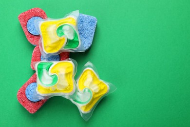 Many dishwasher detergent tablets and pods on green background, flat lay. Space for text