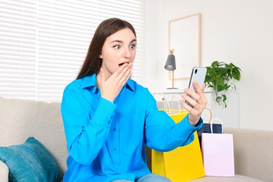 Special Promotion. Emotional young woman looking at smartphone on sofa indoors
