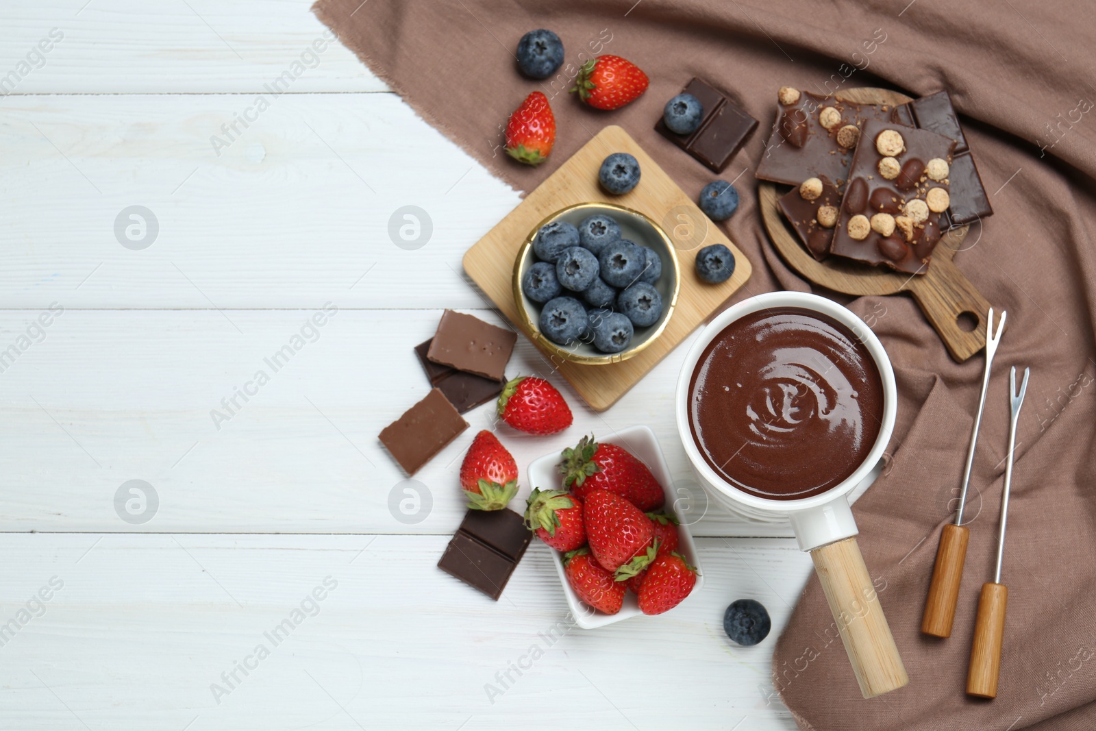 Photo of Fondue pot with chocolate, different berries and forks on white wooden table, flat lay. Space for text