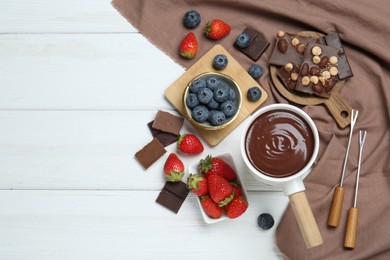 Fondue pot with chocolate, different berries and forks on white wooden table, flat lay. Space for text