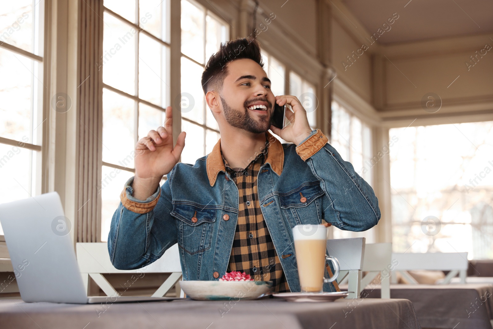 Photo of Young blogger talking on phone at table in cafe