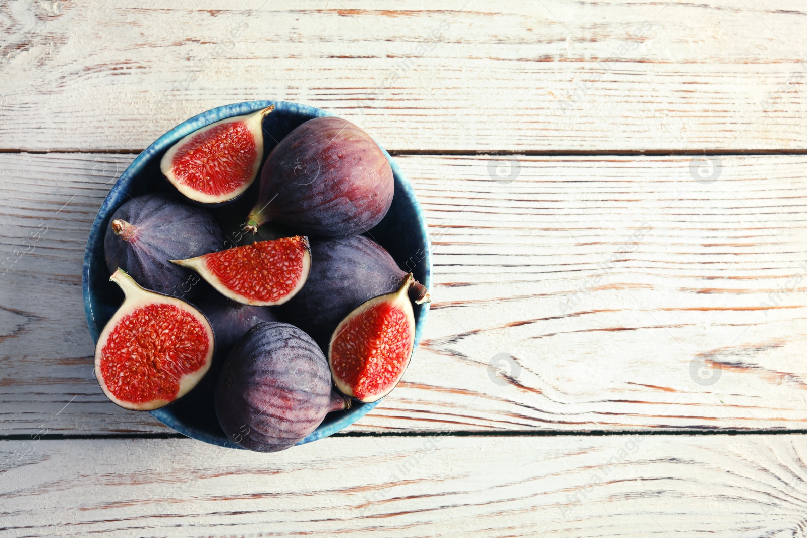 Photo of Bowl with fresh ripe figs on wooden background, top view. Space for text