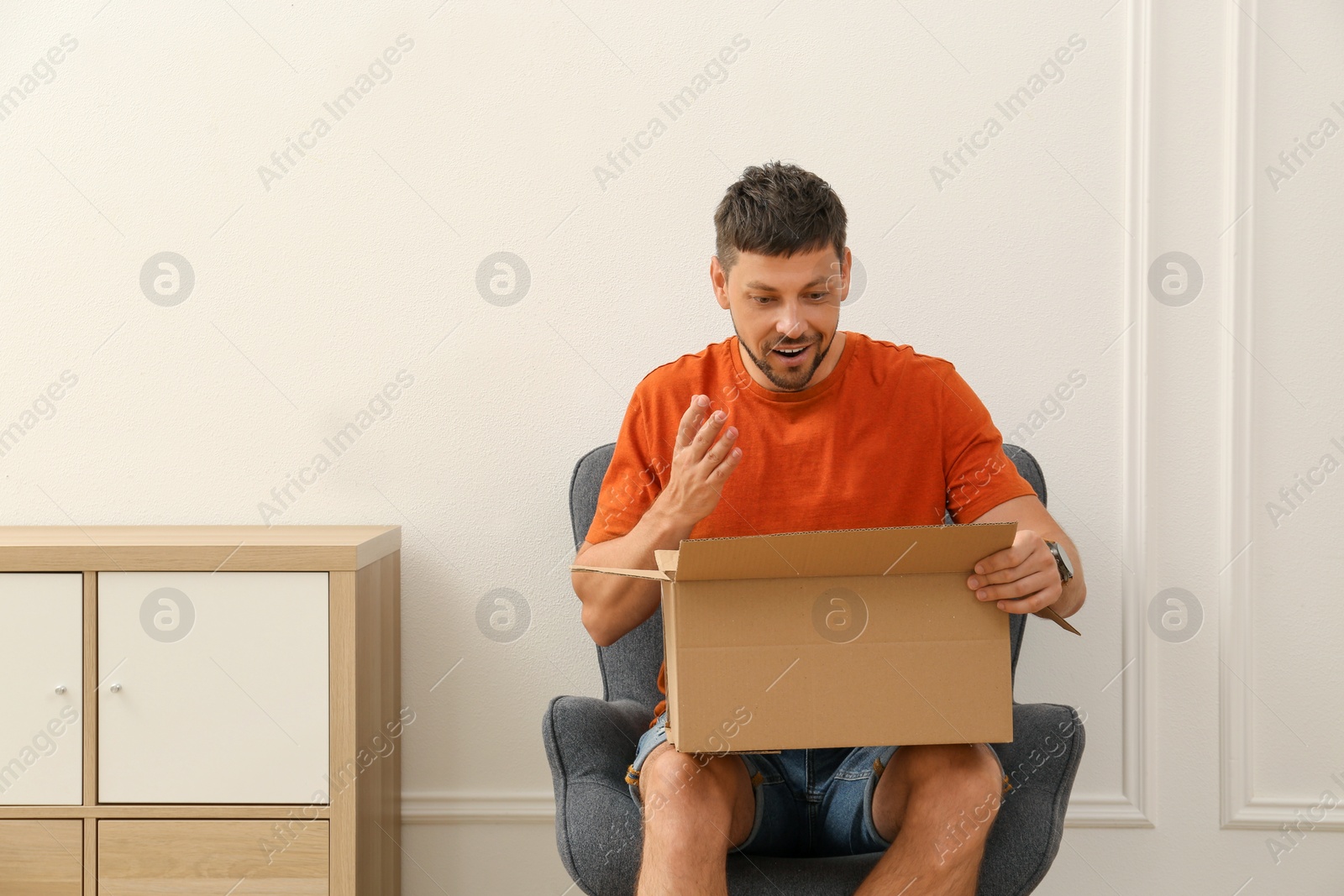 Photo of Happy man opening parcel indoors. Internet shopping