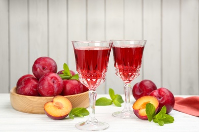 Photo of Delicious plum liquor, ripe fruits and mint on table against white background. Homemade strong alcoholic beverage