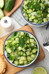 Photo of Bowls of delicious cucumber salad served on light table, flat lay