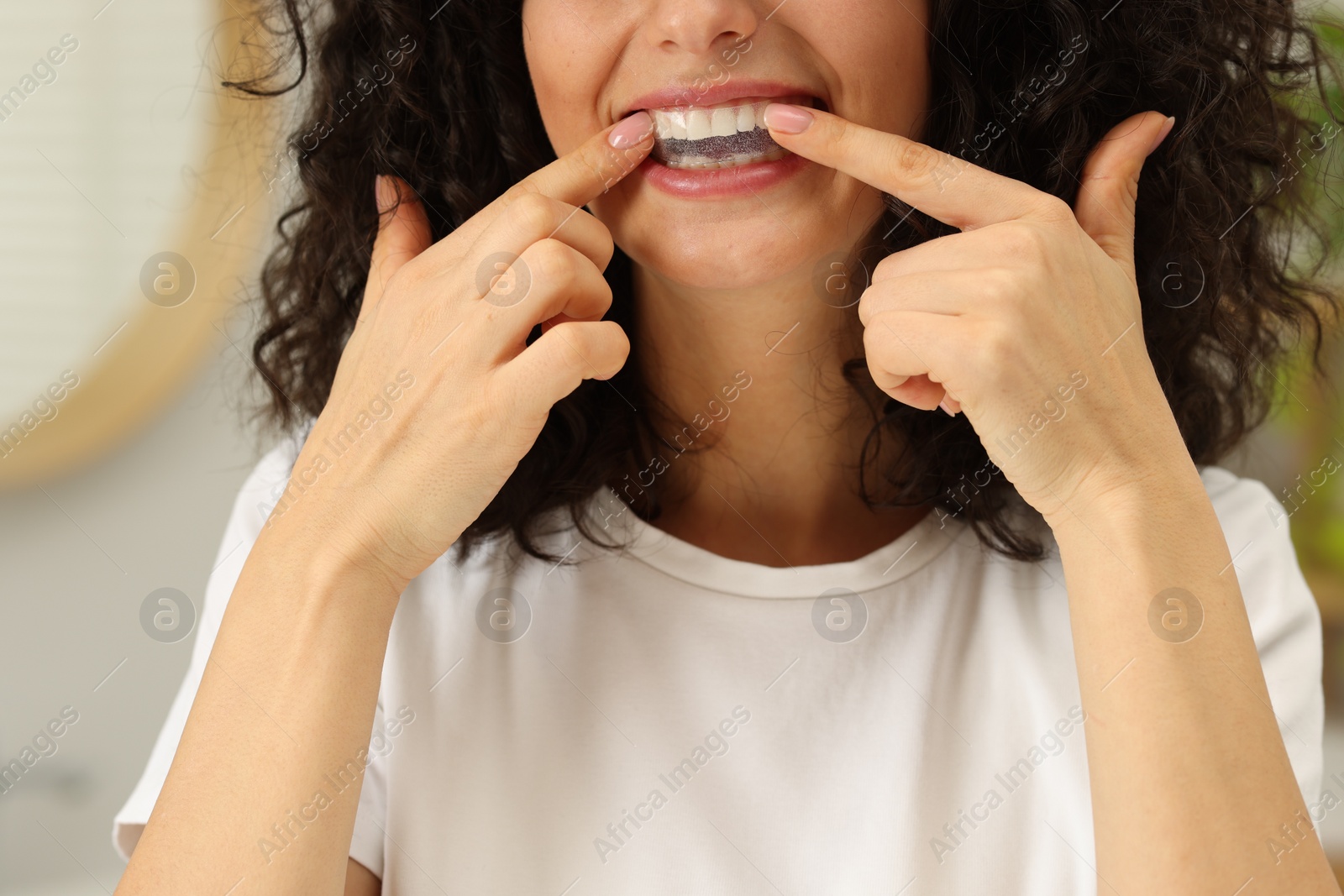 Photo of Young woman applying whitening strip on her teeth indoors, closeup