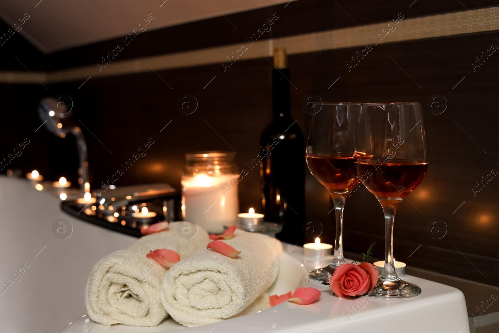 Photo of Glasses of wine, towels and rose on tub in bathroom. Romantic atmosphere