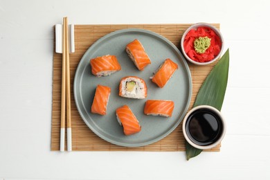 Photo of Delicious sushi rolls with wasabi, soy sauce, ginger and chopsticks served on white wooden table, flat lay