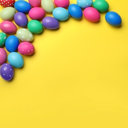 Photo of Bright painted eggs on yellow background, flat lay with space for text. Happy Easter