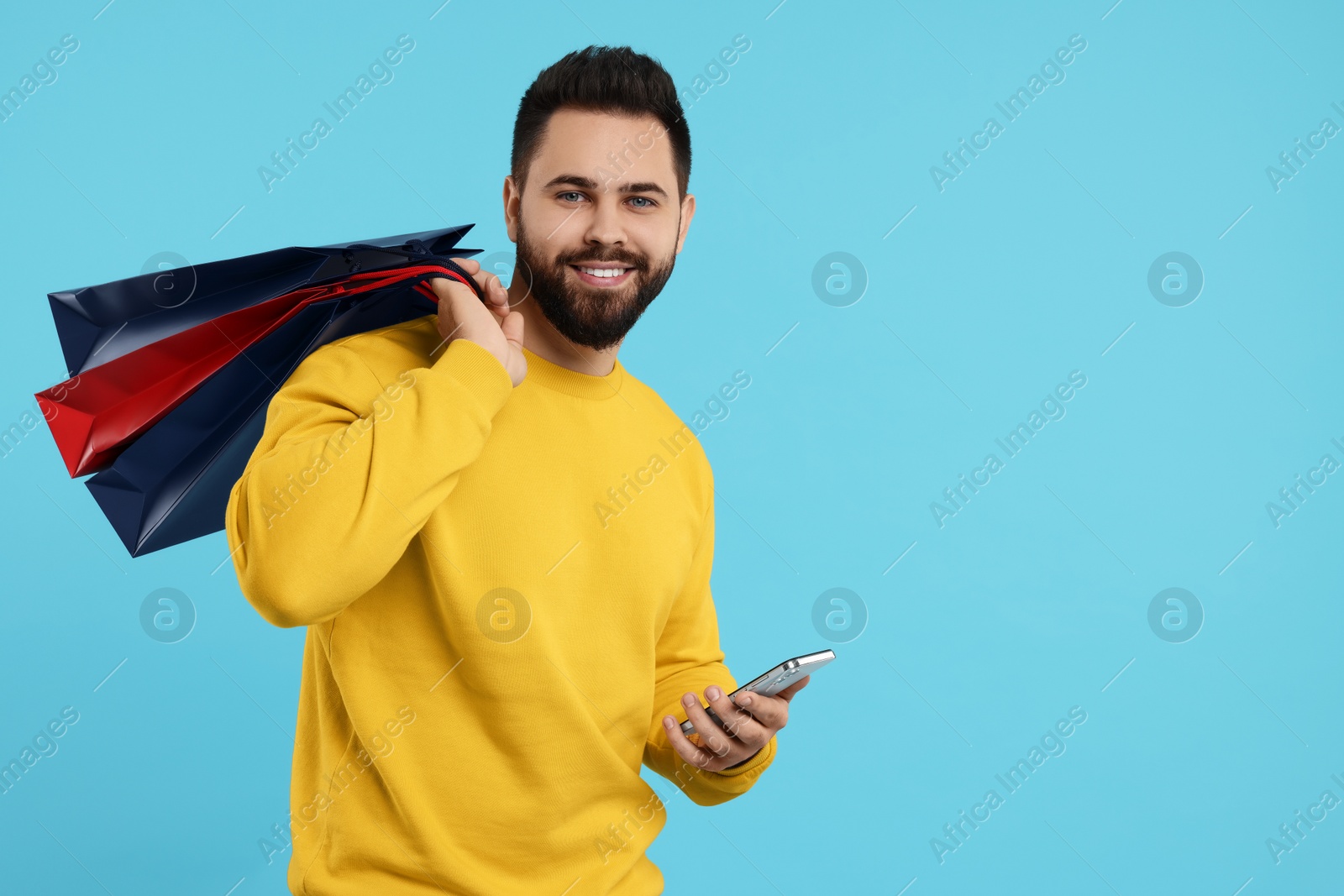 Photo of Smiling man with paper shopping bags and smartphone on light blue background. Space for text