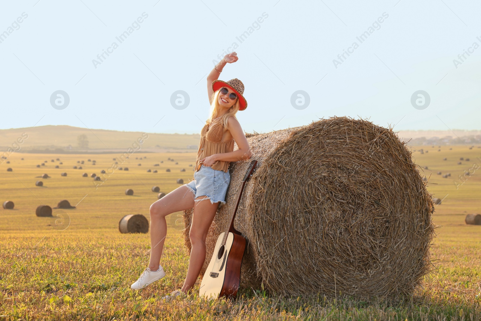 Photo of Happy hippie woman with guitar near hay bale in field