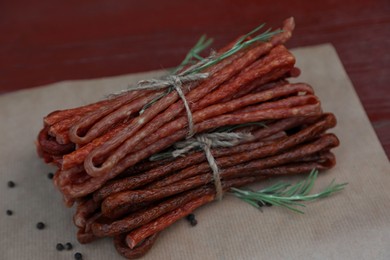 Photo of Tasty dry cured sausages (kabanosy) and spices on parchment paper, closeup