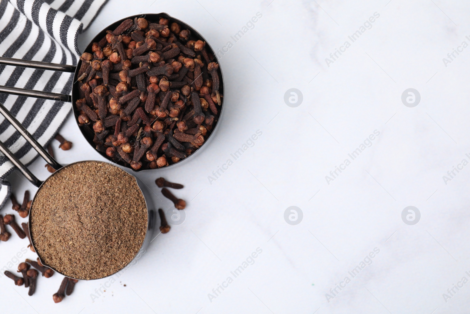 Photo of Aromatic clove powder and dried buds in scoops on white table, top view. Space for text