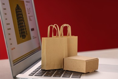 Photo of Mini shopping bags and box on laptop against red background, closeup. Online store