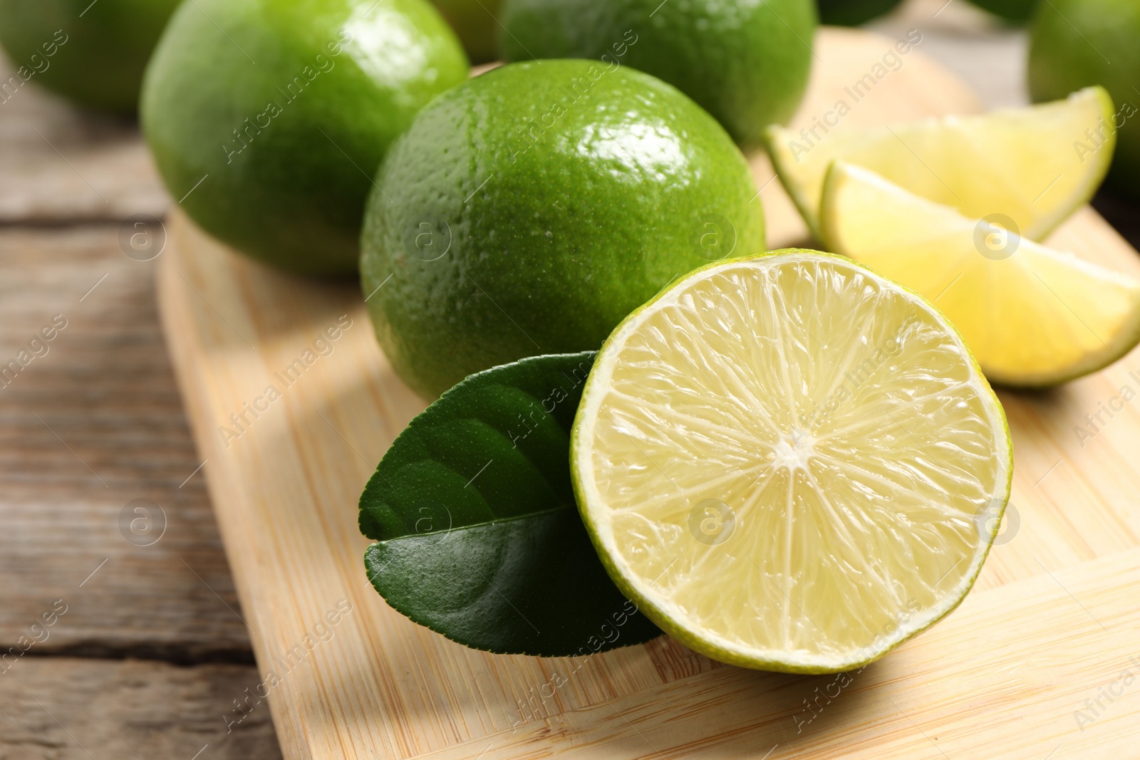 Photo of Whole and cut fresh limes on wooden table, closeup