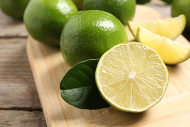 Photo of Whole and cut fresh limes on wooden table, closeup