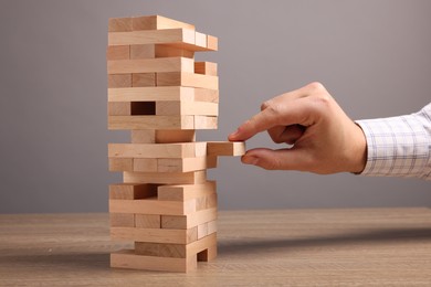 Photo of Playing Jenga. Man removing block from tower at wooden table against grey background, closeup