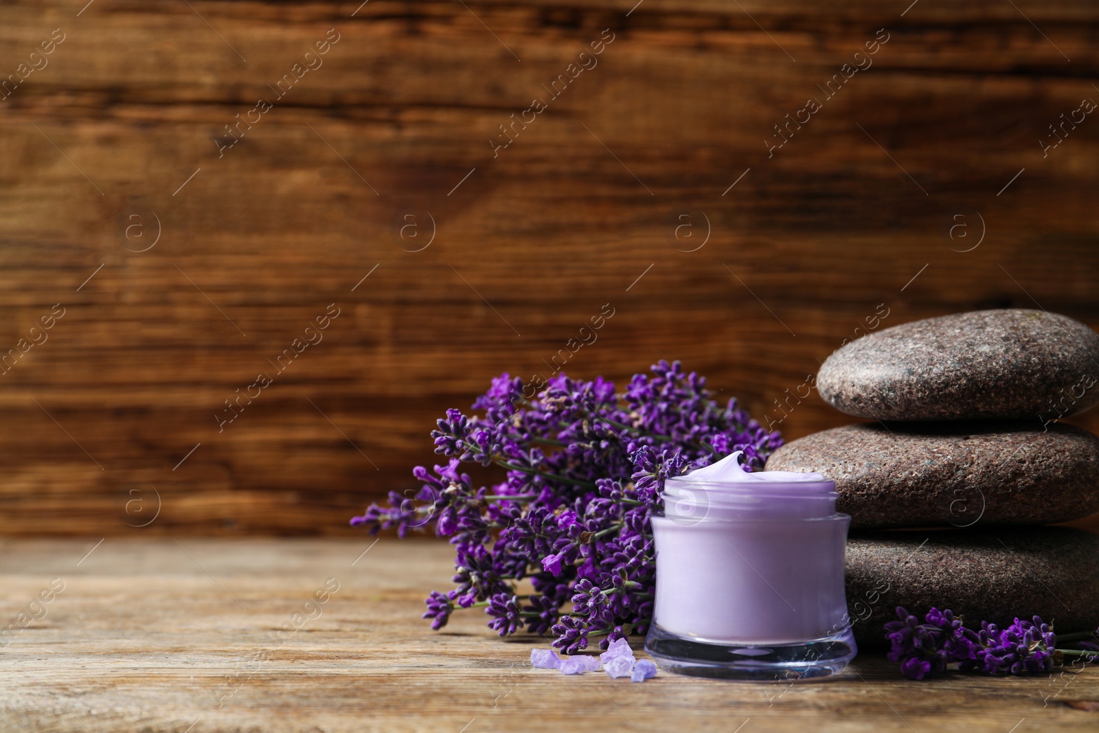 Photo of Stones, jar of cream and lavender flowers on wooden table. Space for text