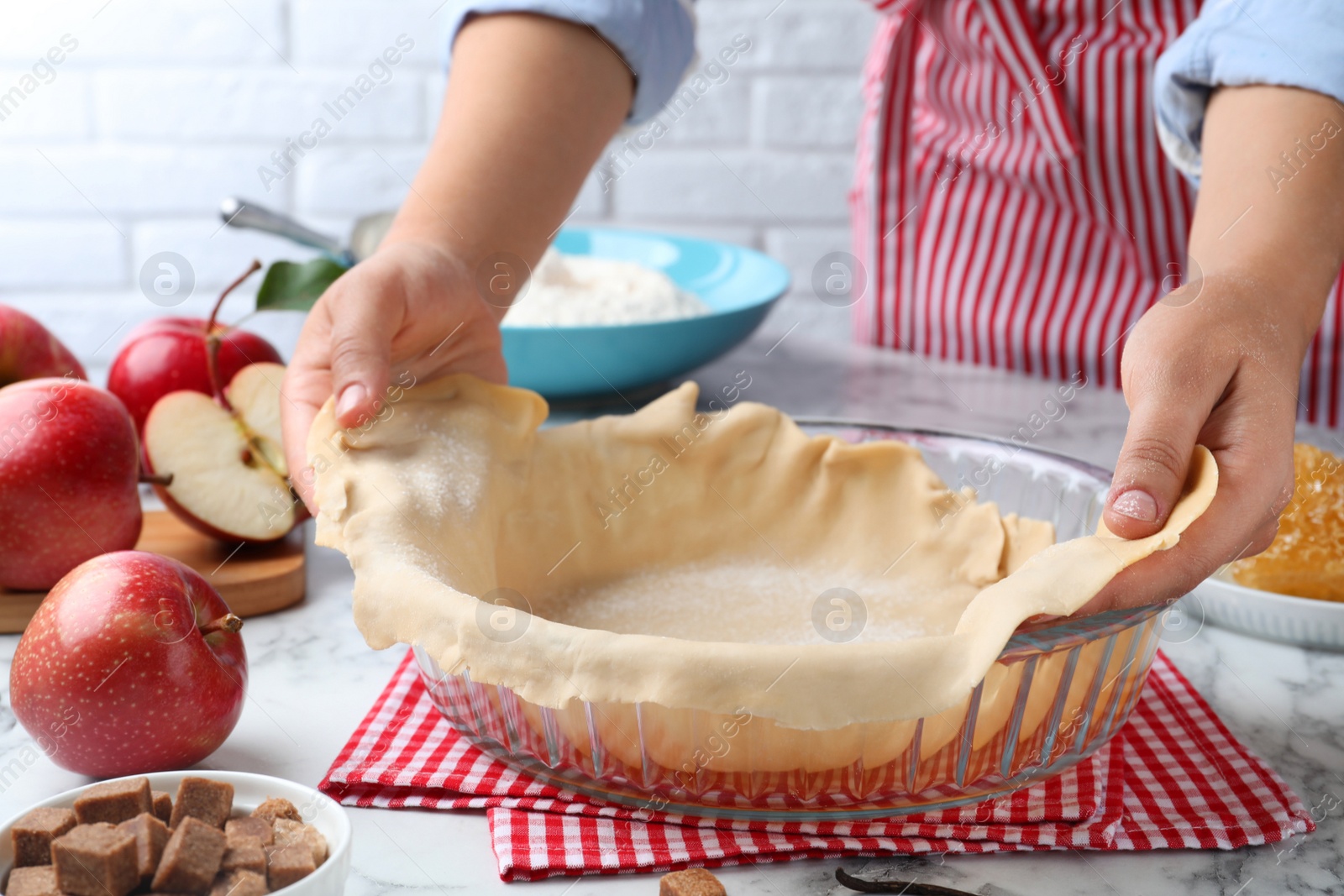 Photo of Woman putting dough for apple pie into baking dish at white marble table, closeup