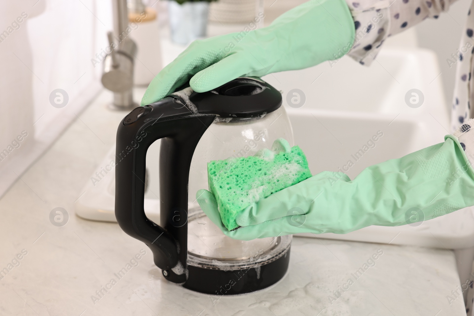 Photo of Woman cleaning electric kettle with sponge at countertop in kitchen, closeup