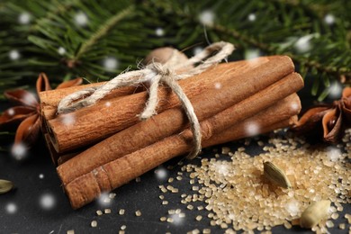 Different spices and fir tree branches on dark table, closeup. Cinnamon, anise, cardamom