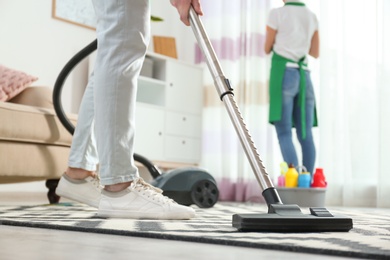 Photo of Cleaning service professional vacuuming carpet indoors, closeup
