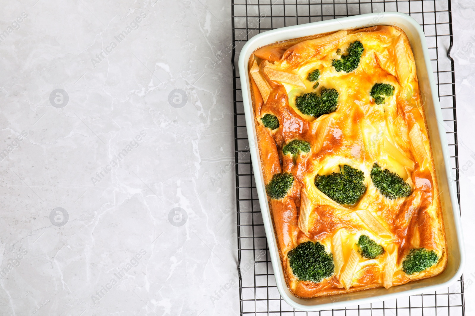 Photo of Tasty broccoli casserole in baking dish on cooling rack, top view. Space for text