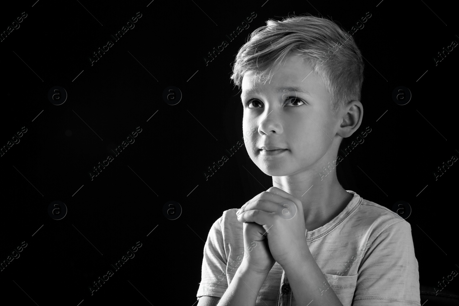 Photo of Little boy with hands clasped together for prayer on dark background, black and white effect. Space for text