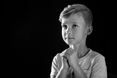 Photo of Little boy with hands clasped together for prayer on dark background, black and white effect. Space for text